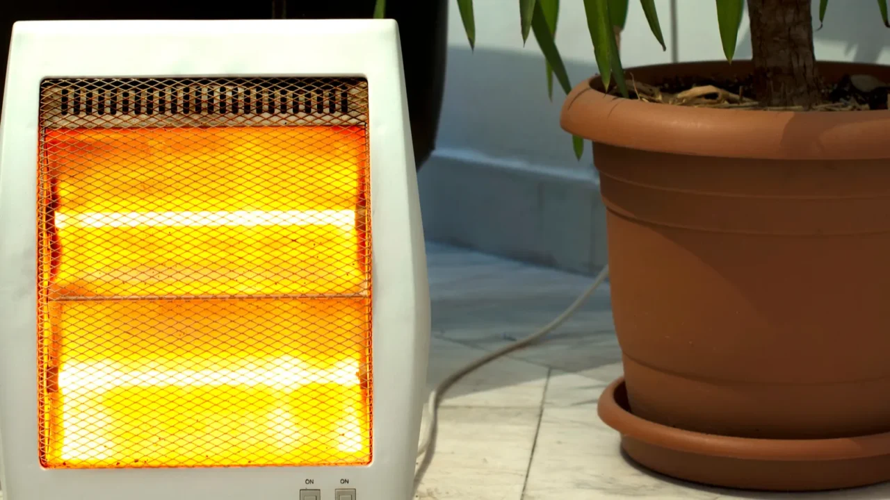 A compact small space heater on the floor with a potted plant beside it.