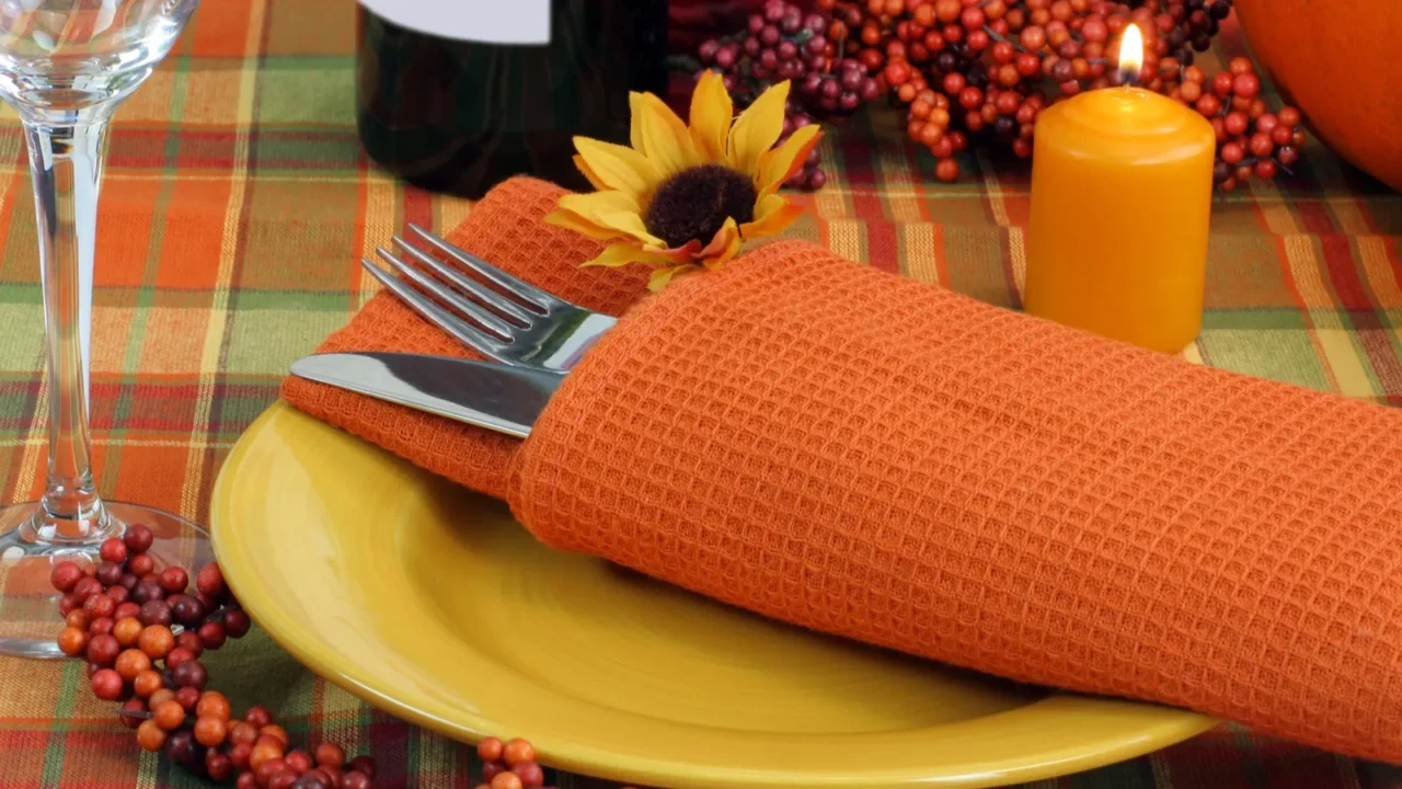 Plait tablecloth with an orange napkin and candle on the table.