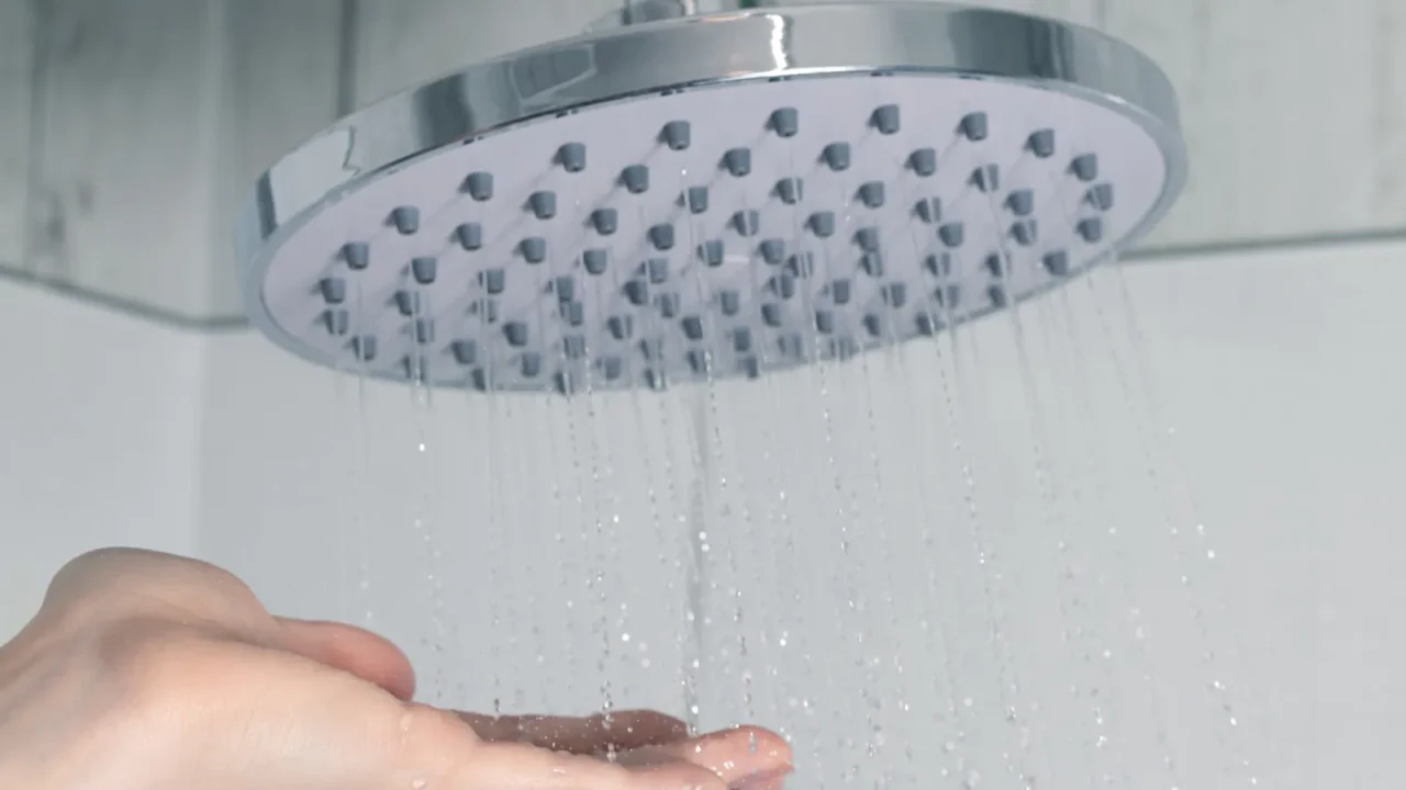 female hand touching water pouring from a rain shower head