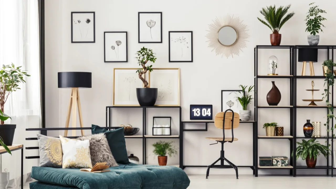 Asymmetrical and black and white living room with a wall covered with bookshelves and decor on it. Wall hanging frames and a navy blue sofa with cushions and plants.