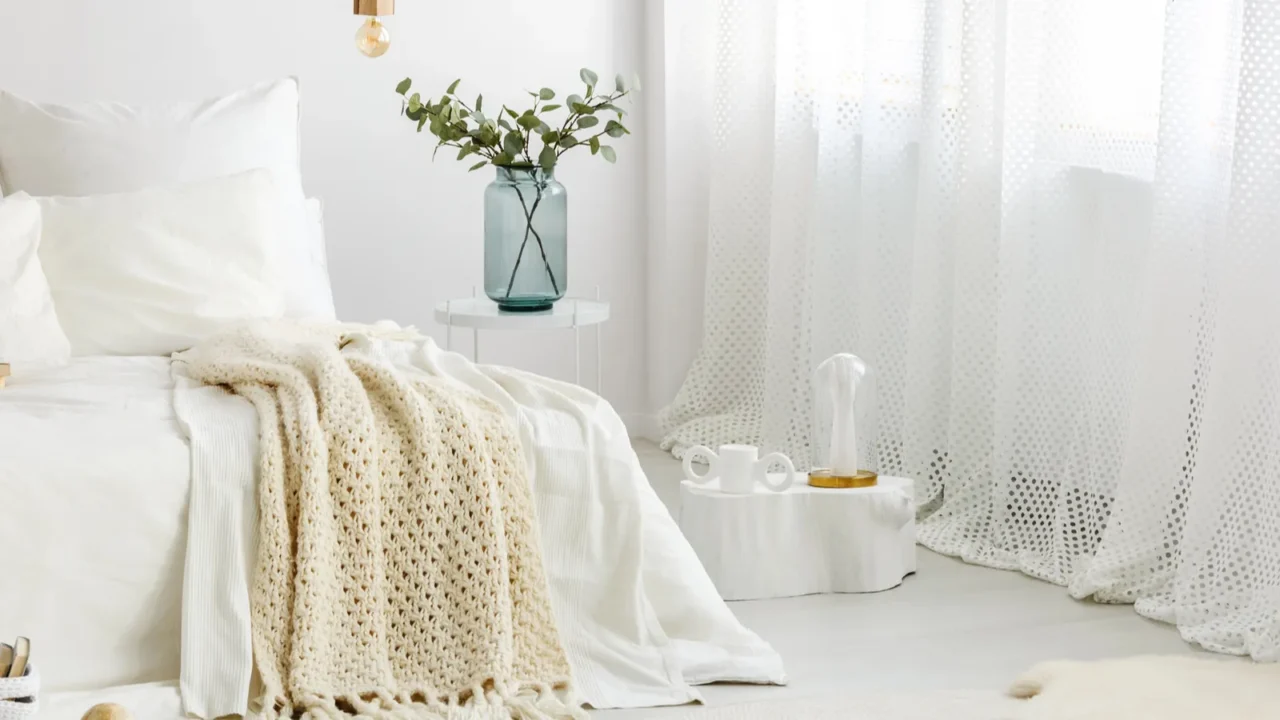 Inspiration for a basic white bedroom interior with cozy textiles, throws, rugs, and thin curtains.