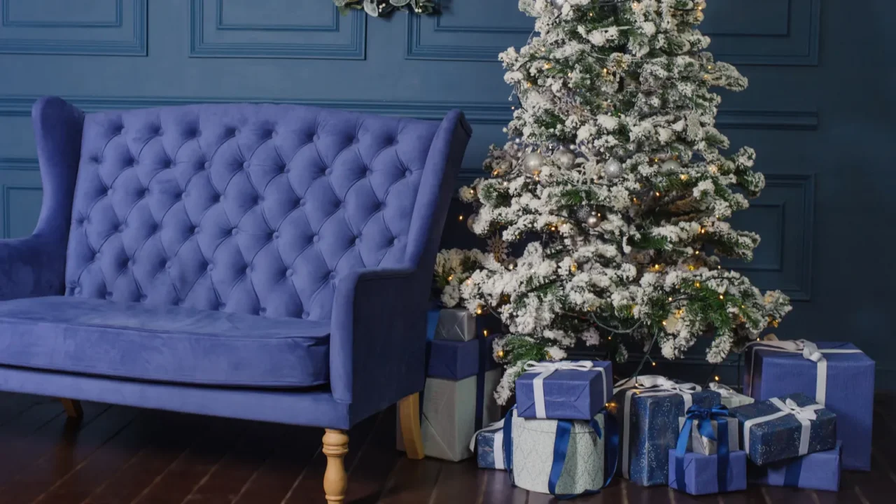 A living room with blue wall, vintage sofa, Christmas tree, and gifts wrapped in blue sheets placed under the tree.