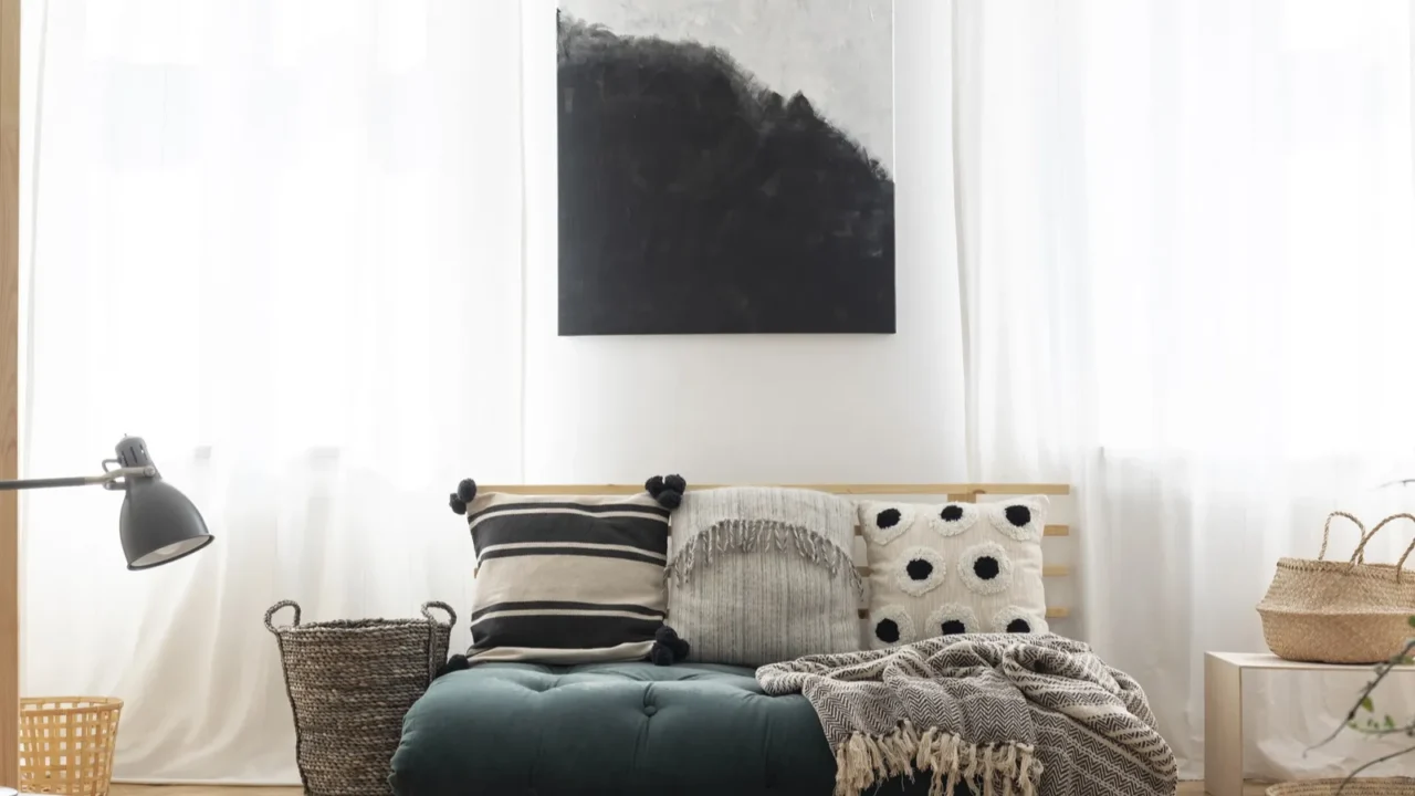 poster above green futon with patterned pillows in bright living