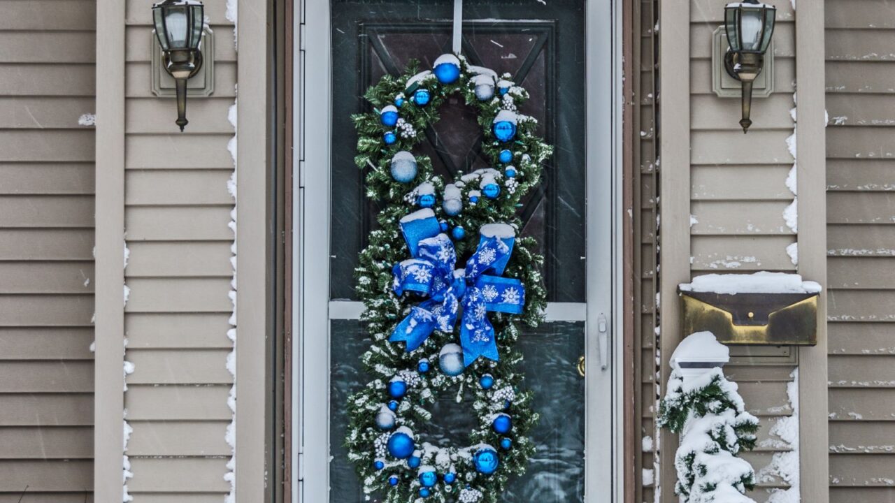 Three green wreaths on a door decorated with blue ornaments and bows for Christmas.