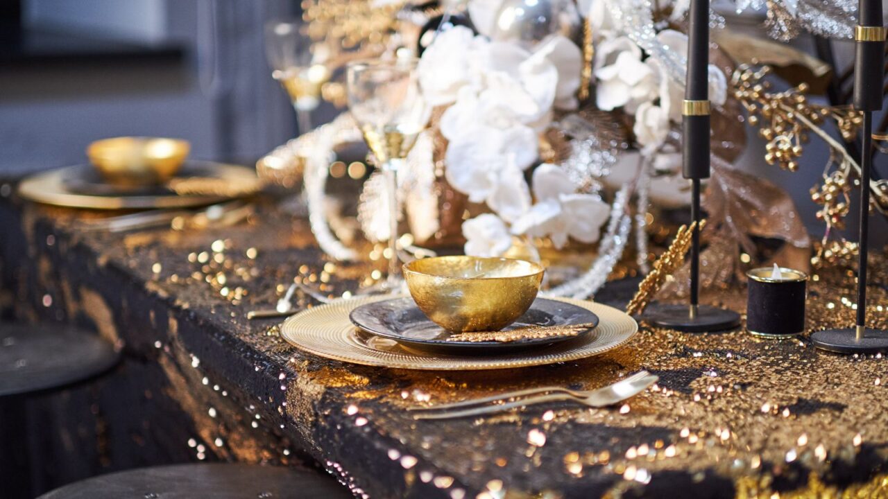 table setting with plates, silverware, gift box and decorations in black and gold colors,