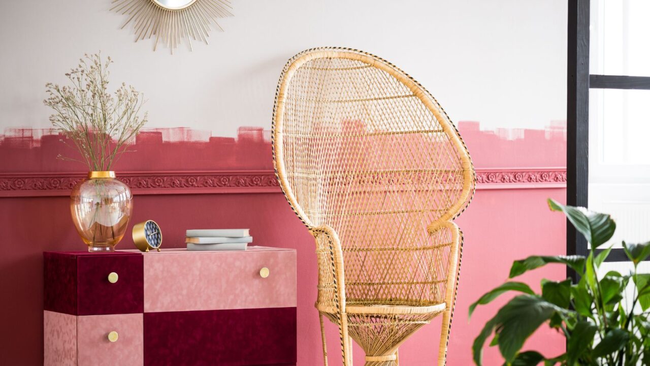 Fashionable living room interior with pink wall and accents and wicker peacock chair.