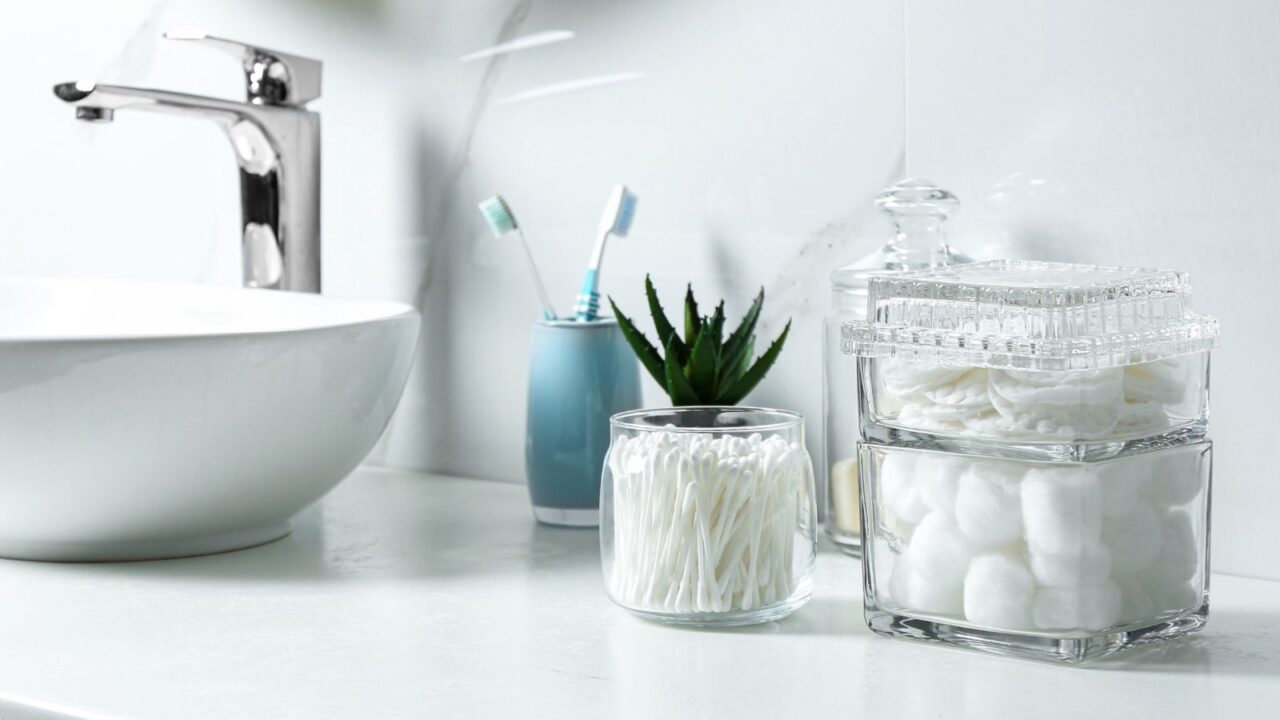 Cotton balls, pads and swabs in stackable clear containers on white countertop in bathroom.