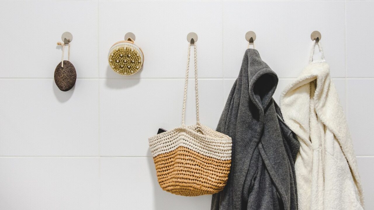 Two bathrobes, a basket and sustainable zero waste bathroom accessories hanging on hooks on a white wall. Sustainable home, plastic free bathroom concept.