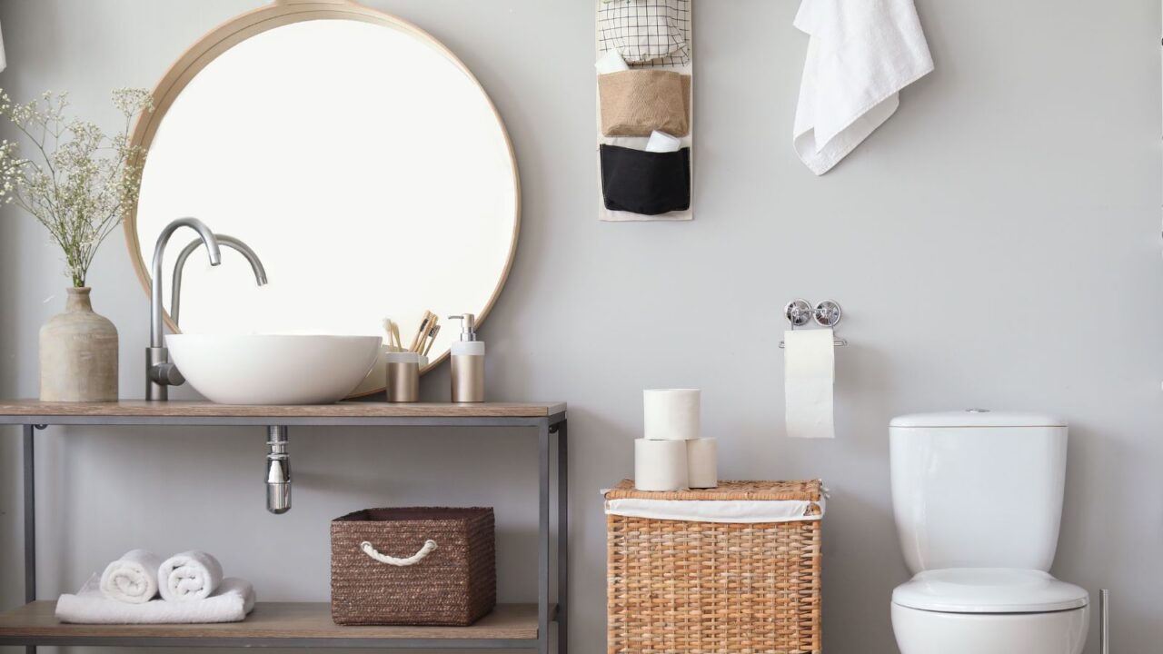 Stylish interior of modern bathroom with toilet bowl, vertical storage solution, rattan basket on the floor, and a basket under sink for storage.