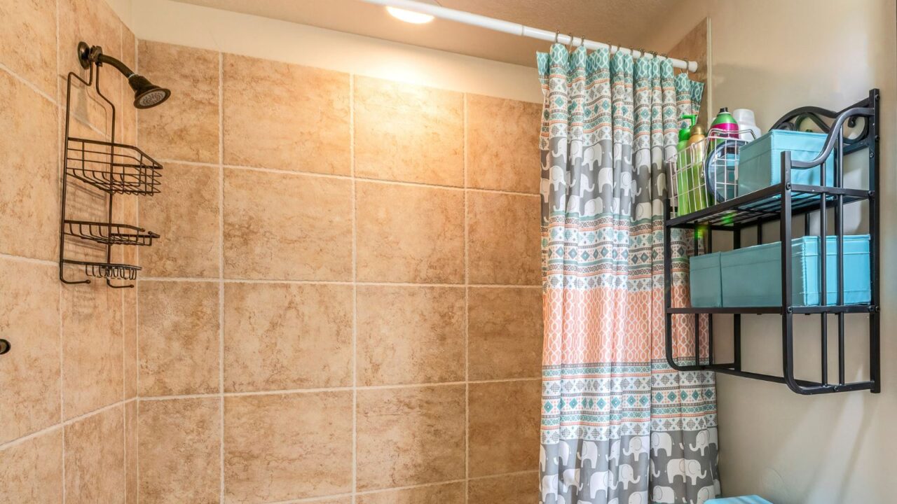 Bathroom interior with antique fixtures and ceramic tile walls. There is a vanity sink beside toilet. Bathtub with shower curtain and caddy.