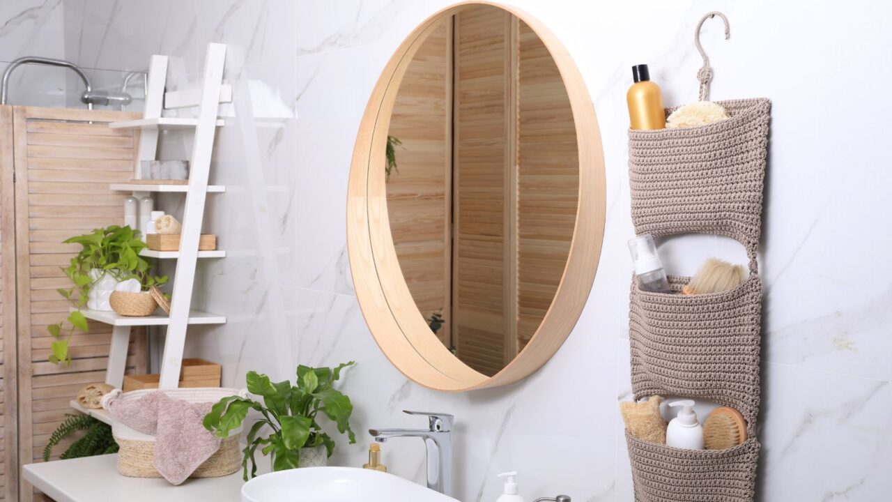 Bathroom interior with essentials and stylish accessories, tiered basket, ladder, and round mirror.