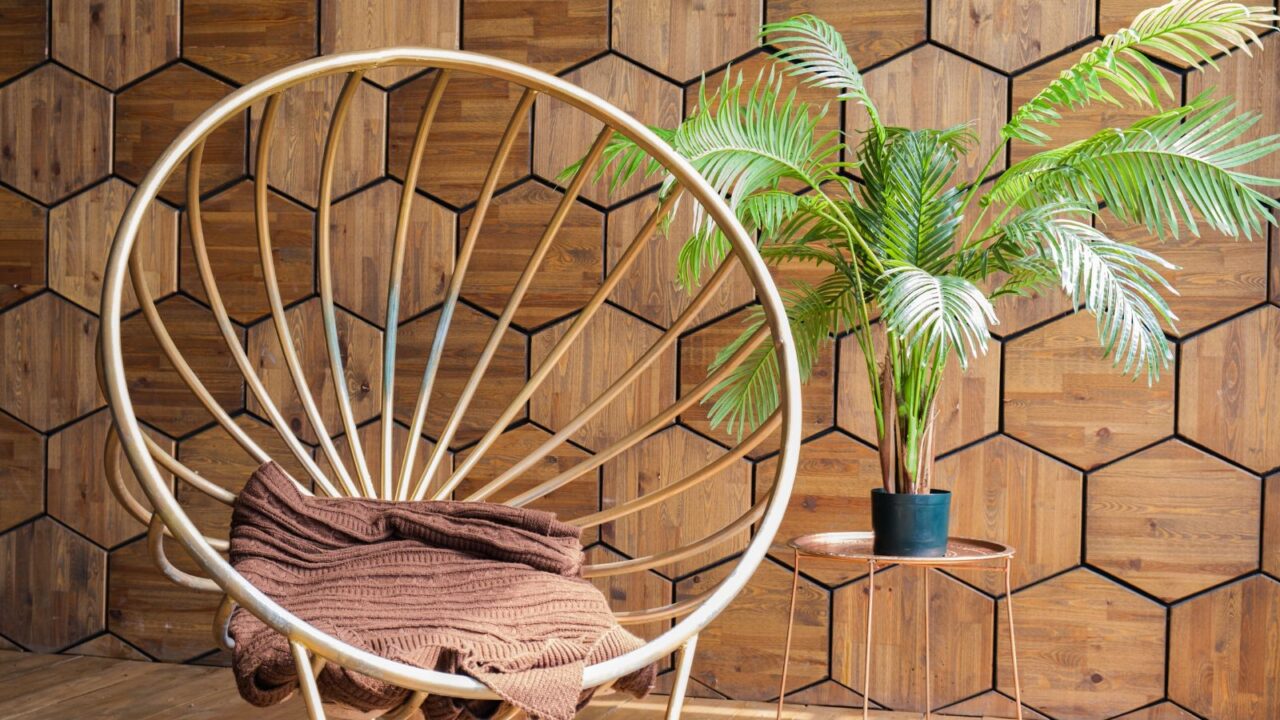 Round metal chair with plaid, coffee table with live houseplant on hexagon wood-panelled wall background. Cozy place to relax, read in the loft. Interior with wooden walls and floors.