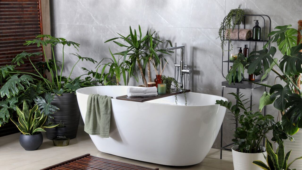 Modern white tub and beautiful green houseplants in bathroom. Interior design.