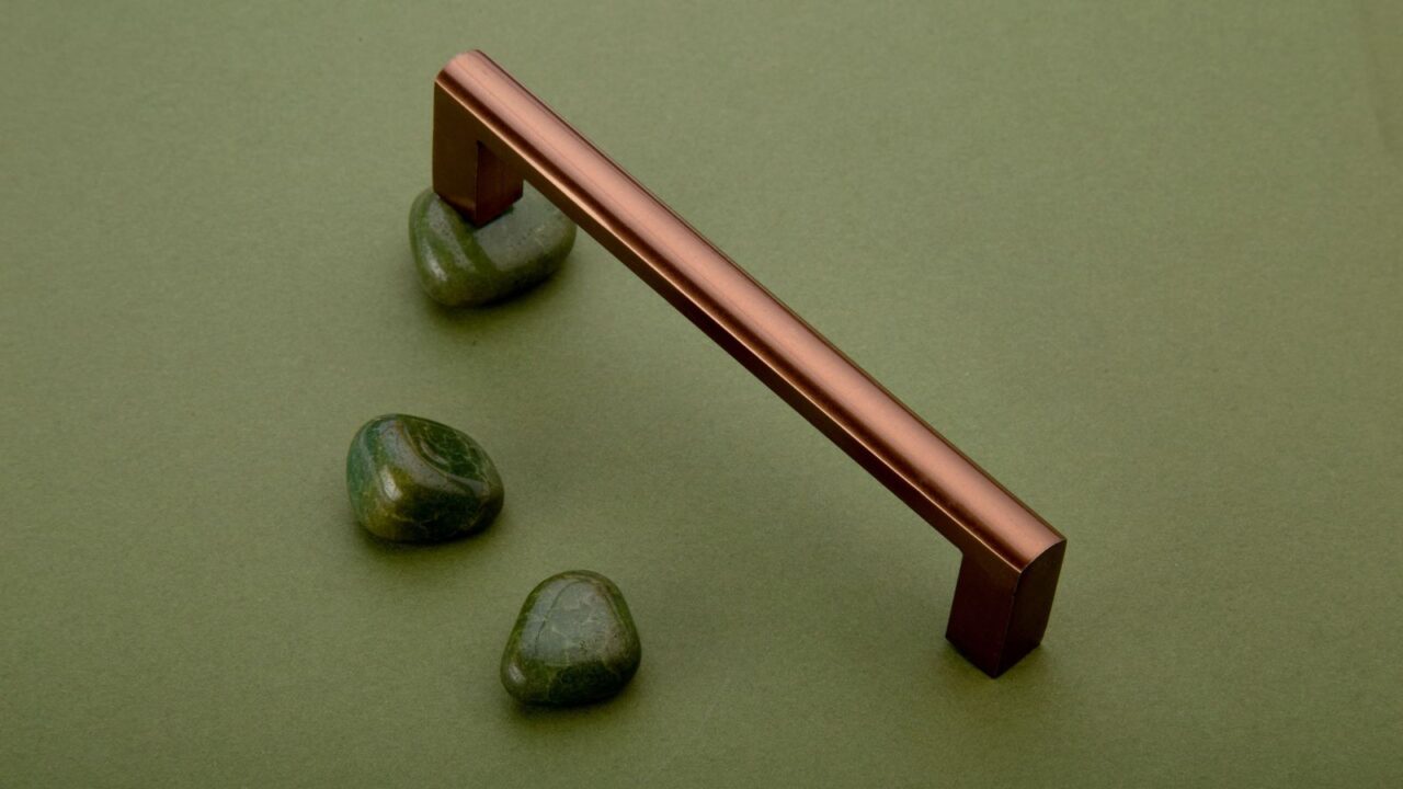 A shiny copper pull handles and green natural stones on green surface.