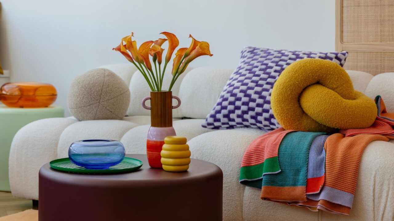 Colorful and cozy living room with vibrant cushions, colorful throw, and colorful decor accents and flowers in a vase on a coffee table.