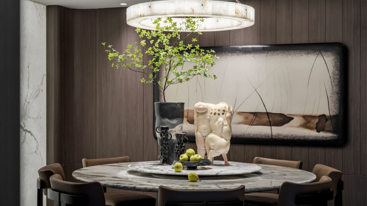 Round table with marble top, decorative pears, big sculptures, vase with branches, and circular ceiling light.