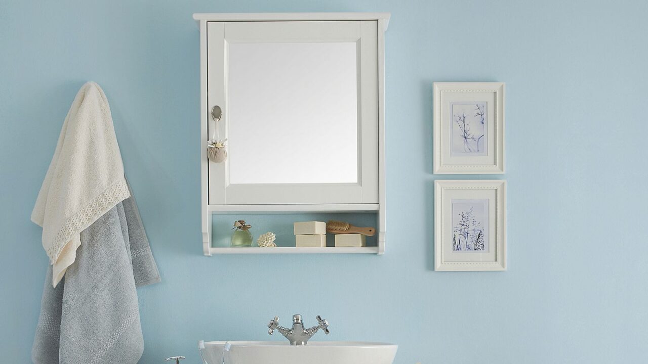 Bathroom interior with blue wall, mirror cabinet, towers hanging on a hook, and 2 frames on the right above the sink.