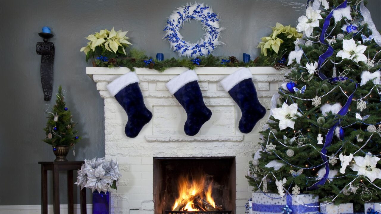 Landscape Christmas background with blue tree and decorations around fire. Navy velvet stockings hanging on the mantel and wreath hanging on the wall.