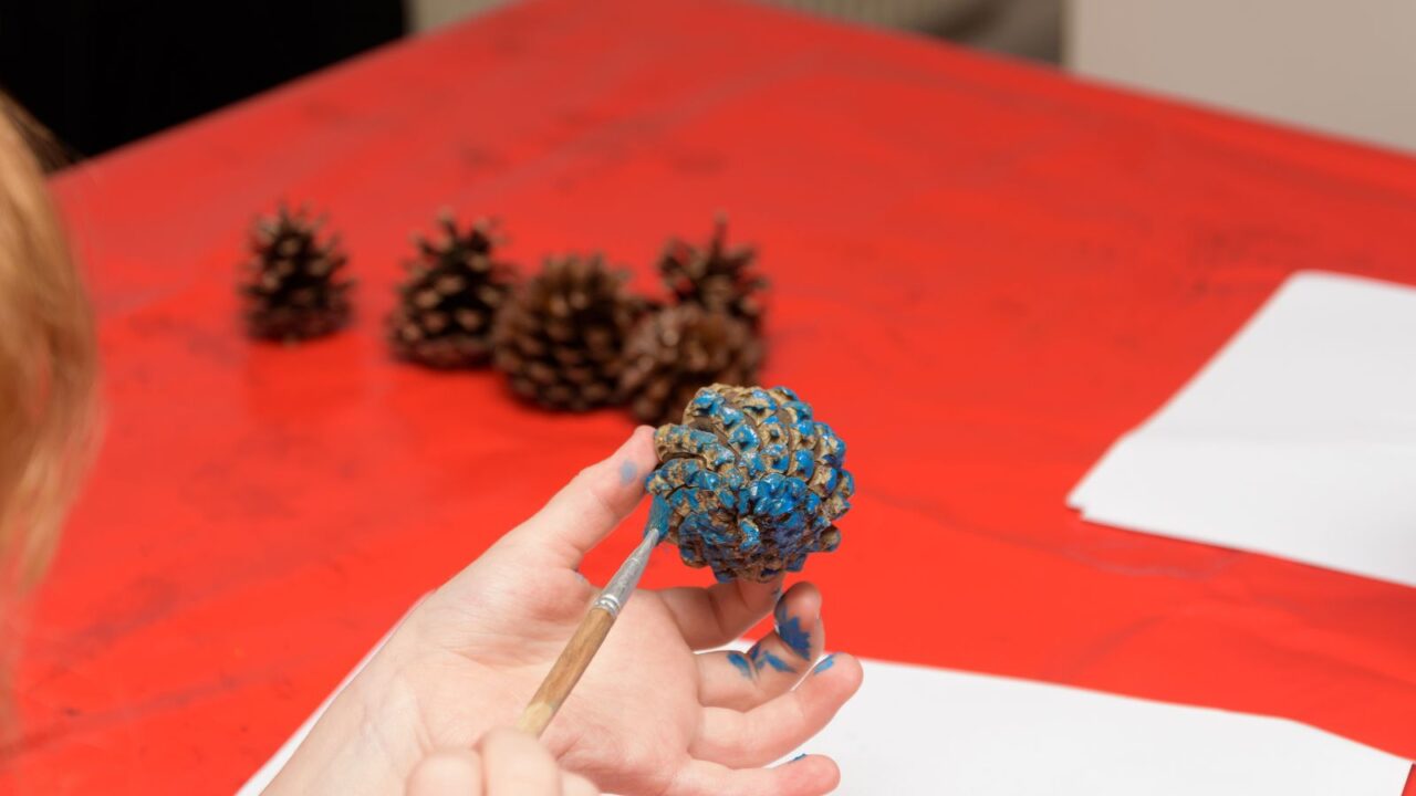 A child painting a pinecone for blue Christmas decoration.