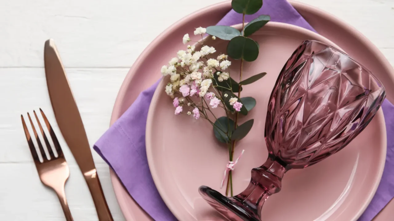 Stylish table setting and flowers on light wooden background. Pink dinnerware plates and glasses.