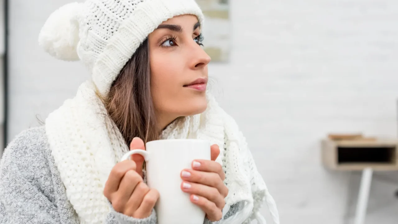 thoughtful young woman in warm clothes holding cup of hot