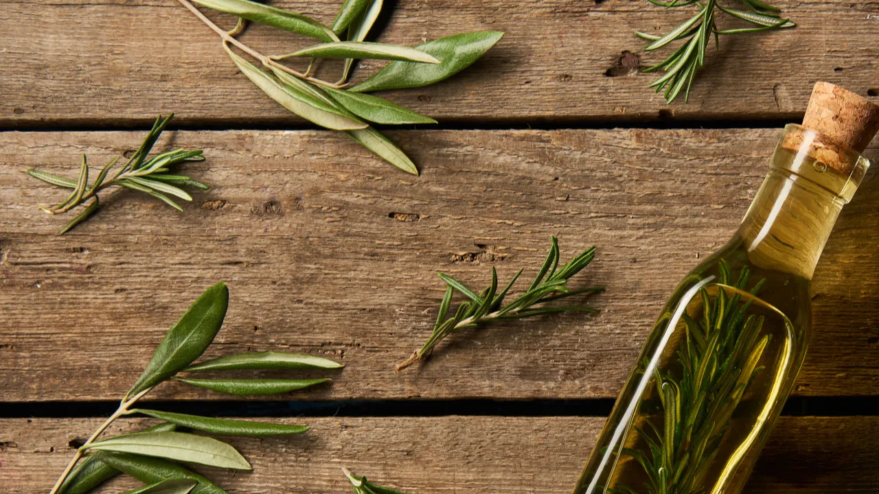 Top view of bottle with flavored oil and rosemary branches on wooden background.