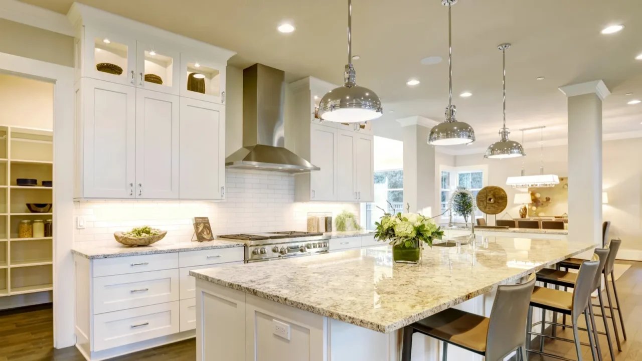 A beautiful white kitchen interior with granite counterop, white cabinets, stainless steel stove and range hood, and tile backsplash.