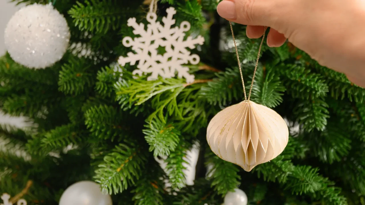 Image shows a person's hand decorating Christmas tree with paper DIY decor