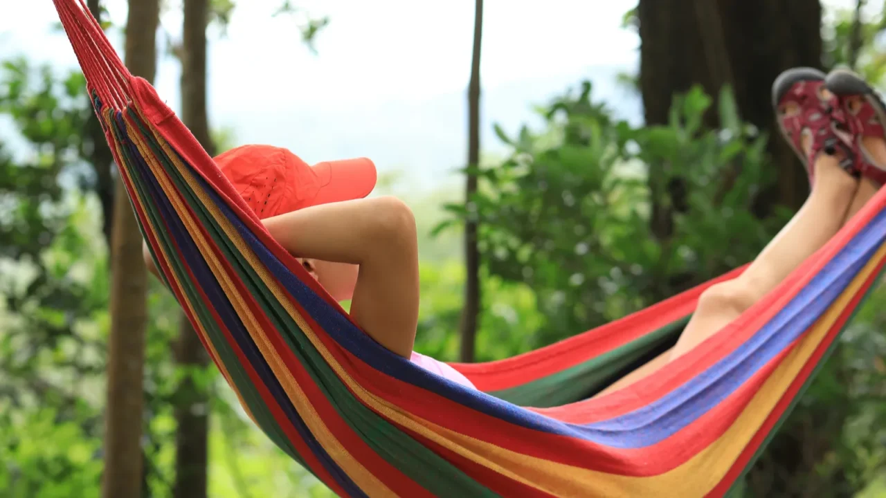 Woman relaxing in a colorful Brazilian hammock in summer forest.