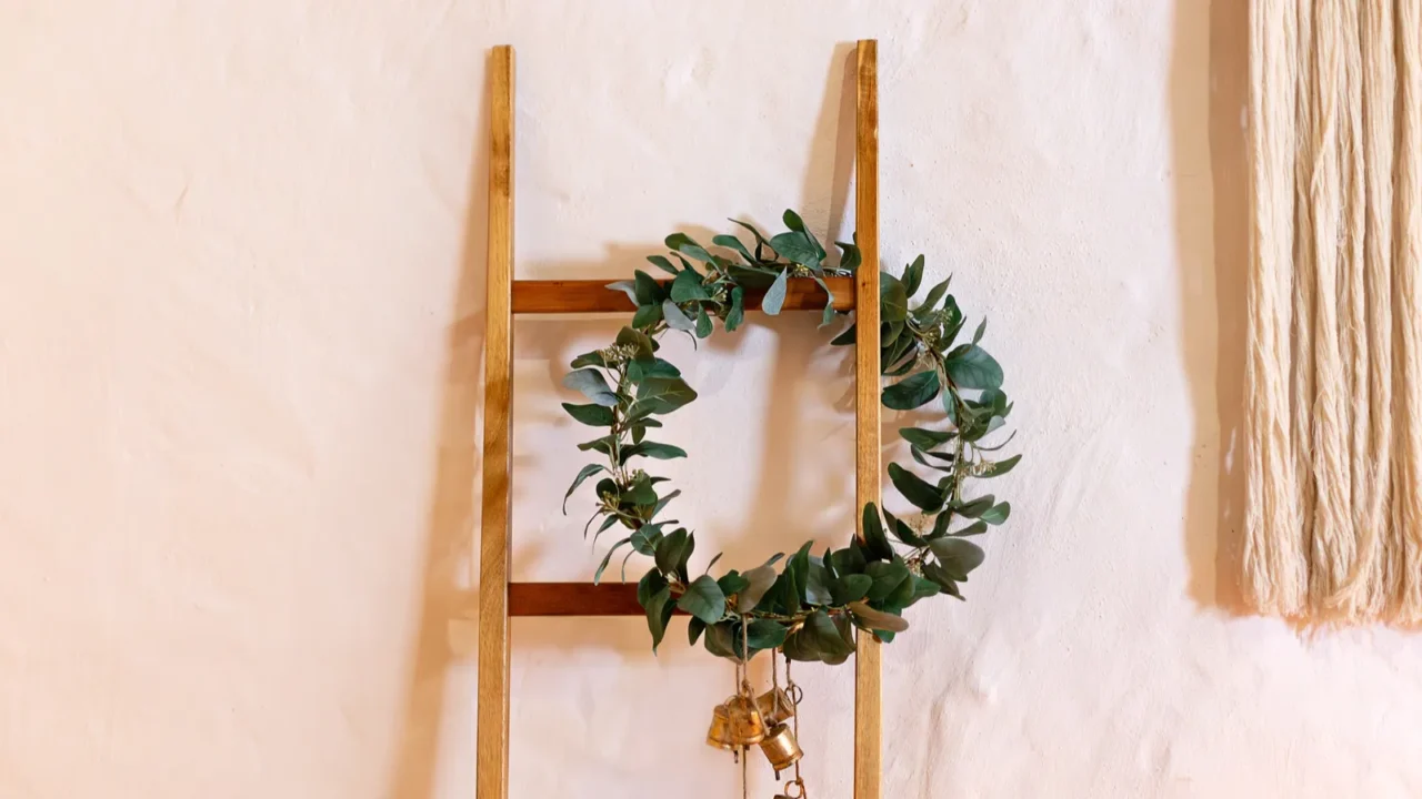 Wooden ladder against a white wall boxwood wreath hanging on.