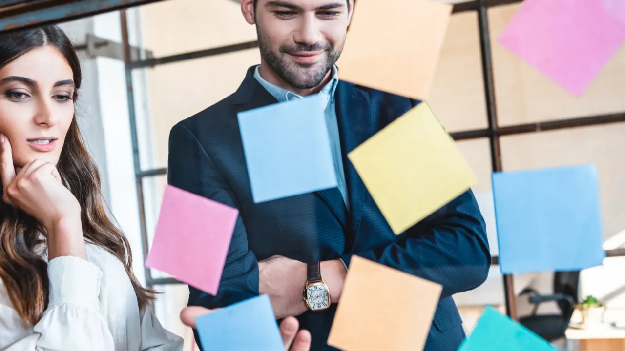 young business colleagues looking at colorful sticky notes at workplace