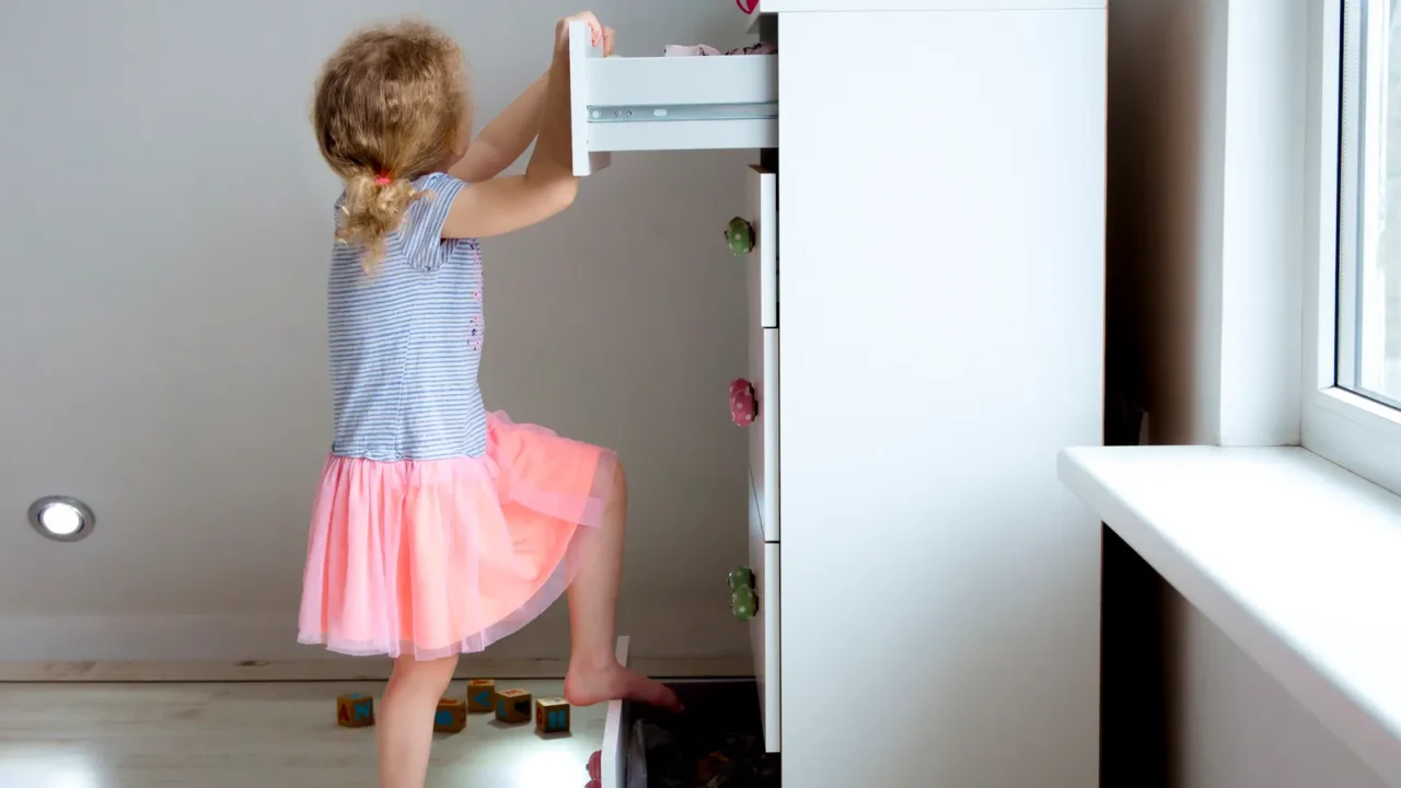 young girl child climbing on modern high dresser furniture danger