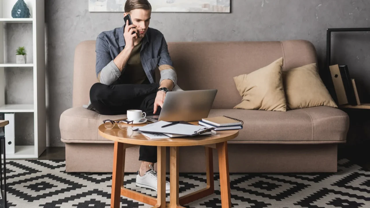 young handsome man working with laptop on couch and talking