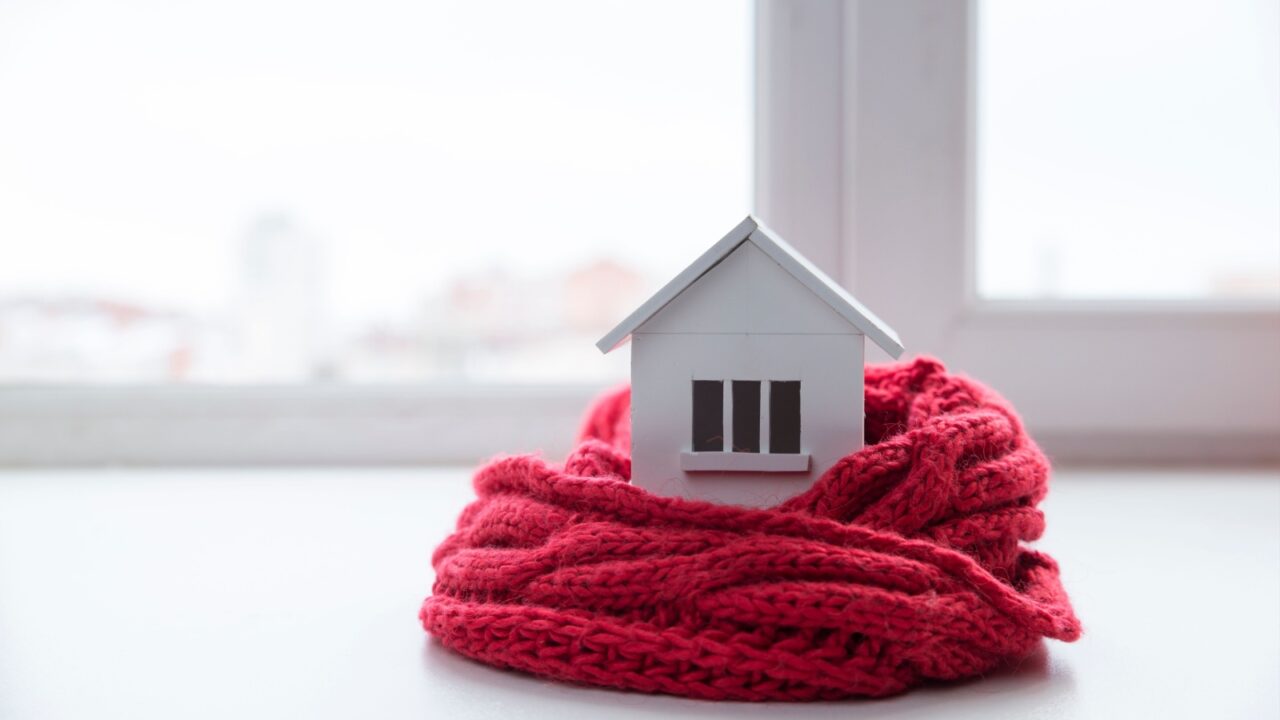 Home insulation concept with model of a house wrapped in a knitted cap on a window sil.