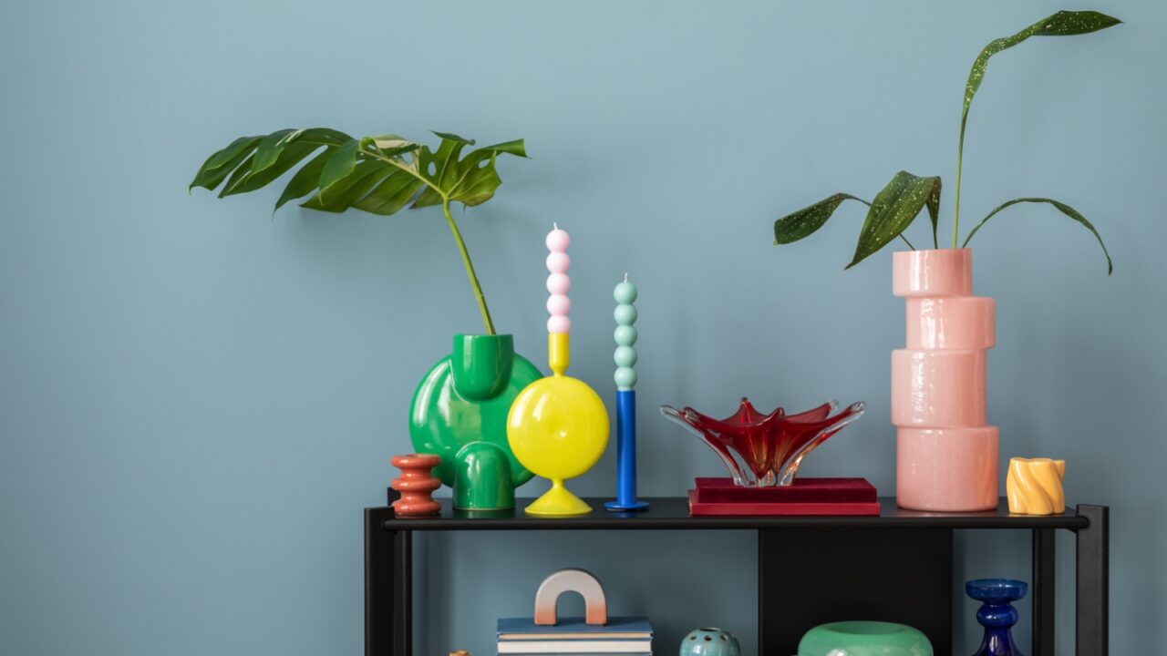 A black shelf with colorful vases, candles, and decor accents in front of a blue wall.