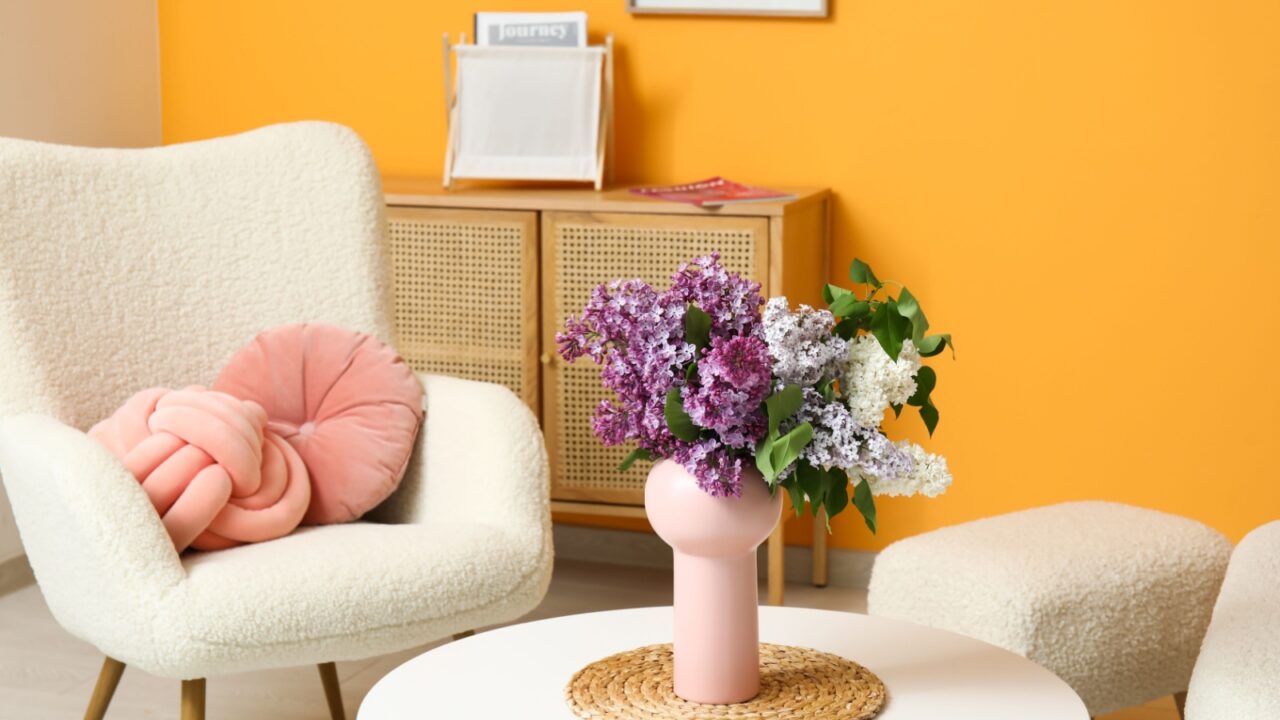 A living room with cozy armchair with decorative cushions and a flower vase on a coffee table.