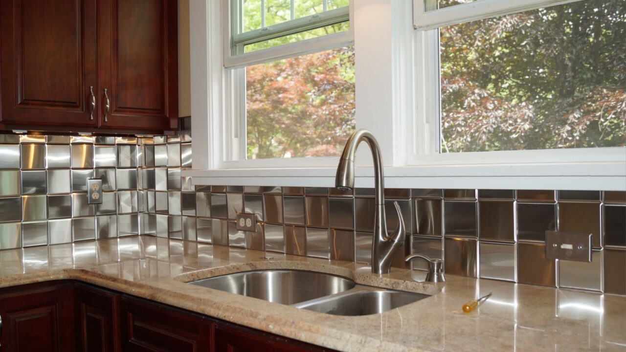 A kitchen interior with steel backsplash, wooden cabinetry, and granite countertop.