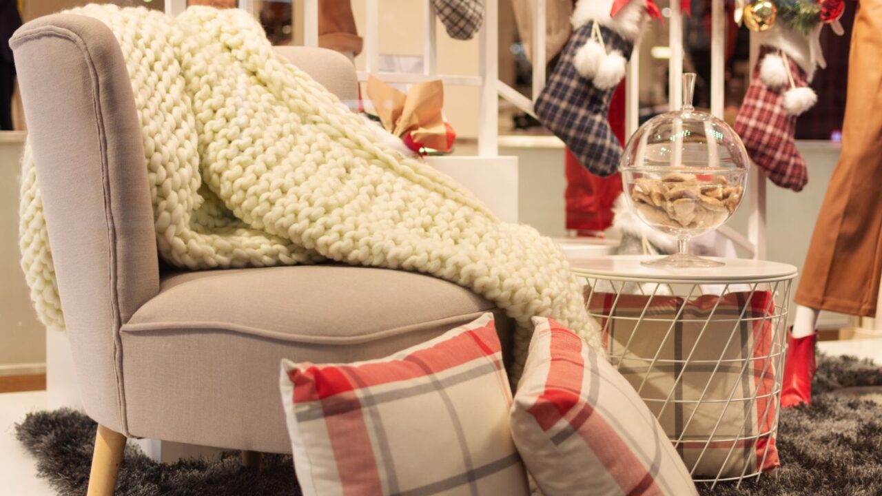 A cozy living room interior with sofa with knitted throw blanket, plaid cushions, fluffy rug, and coffee table.