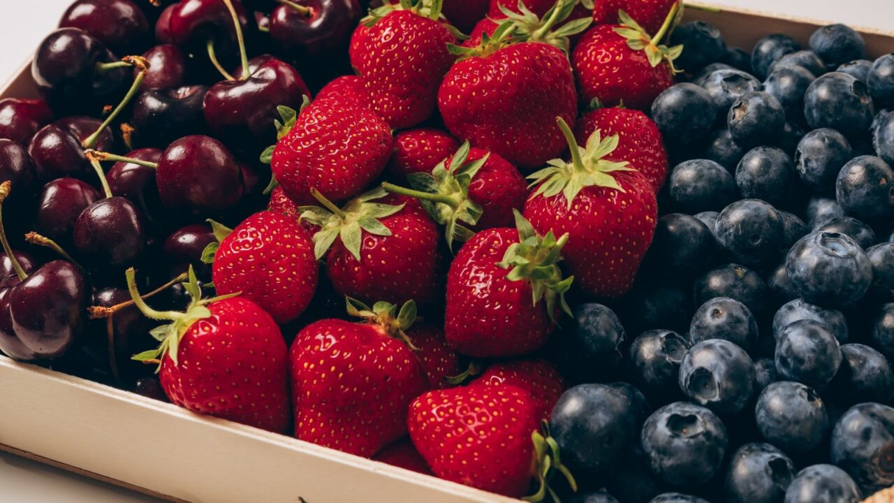 A tray filled with fresh strawberries, blueberries, and cherries.