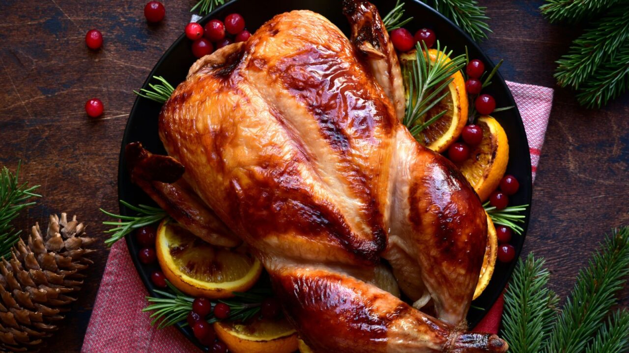 A roasted turkey on a black serving dish with oranges ,rosemary and cranberries on a wooden table.