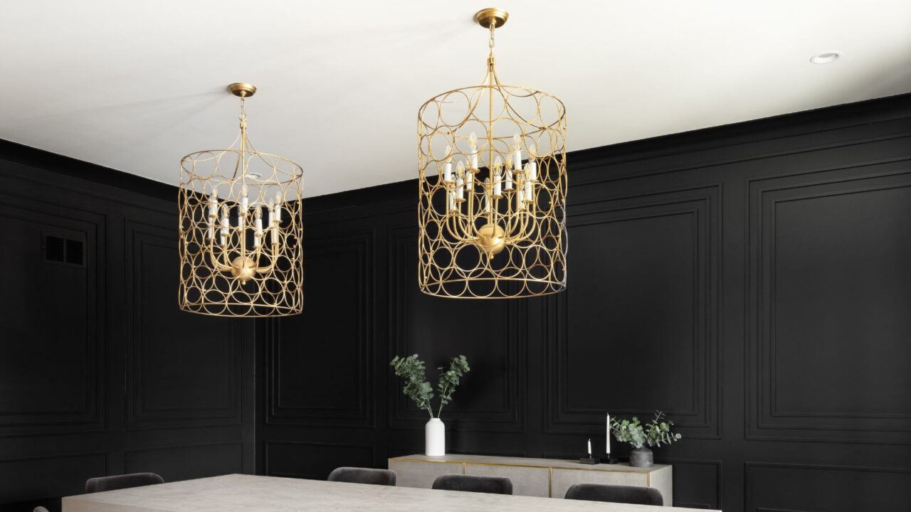 A dining room interior with black walls, console table, and gold chandeliers hanging from the white ceiling.