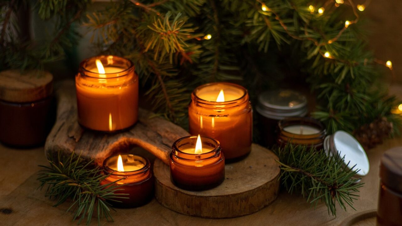 Burning scented candles, plants, and string lights on a wooden table.