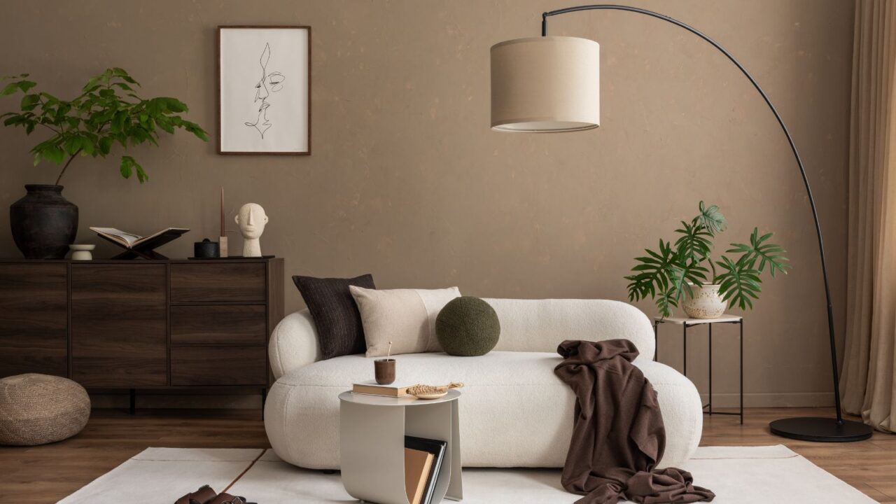 A living room interior with a cozy white sofa, coffee table, wooden console, potted plants, floor lamp, and neutral decor accents.