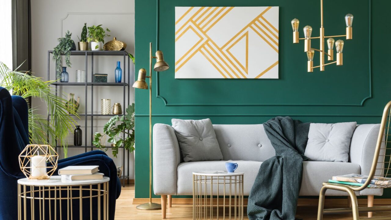 A modern living room with a green accent wall, a grey sofa, gold decor elements, and a geometric wall art piece.