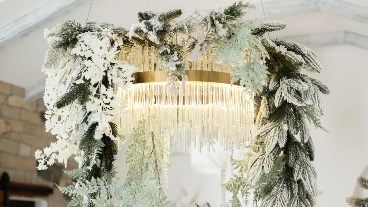 a beautifully designed chandelier features lush greenery and frosted accents