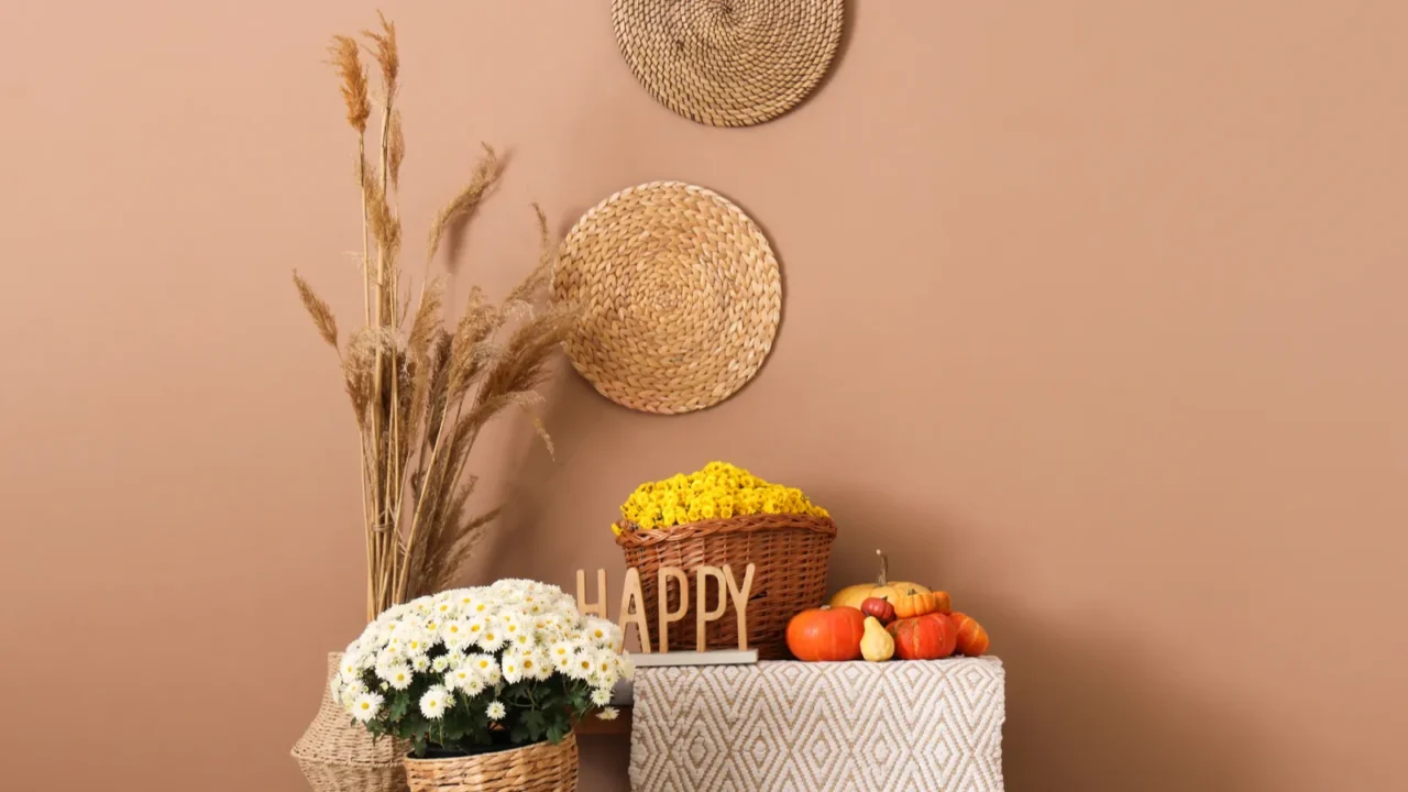 Basket with chrysanthemums, pumpkins, and pouf in front of a beige wall.