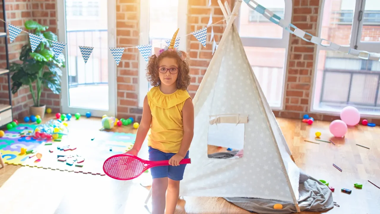 beautiful toddler standing wearing glasses and unicorn diadem playing with