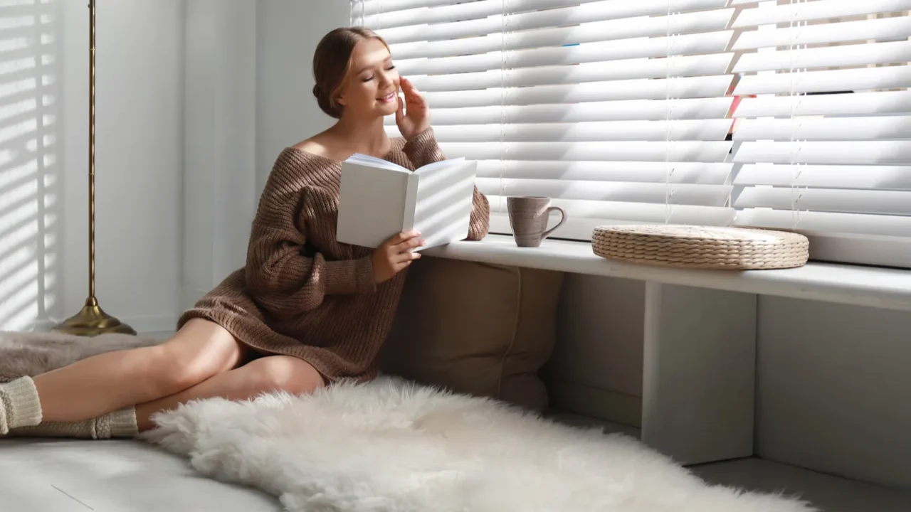 beautiful young woman reading book near window at home winter