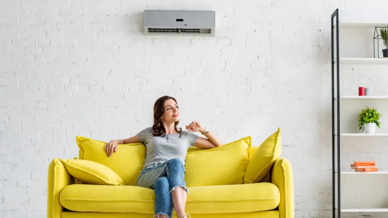 beautiful young woman sitting on yellow sofa under air conditioner