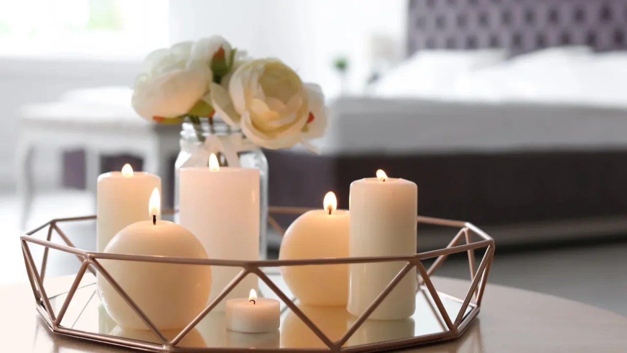 Burning white candles and flowers in a vase on a decorative tray.